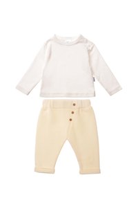 Cremfarbener Langarm-Top mit Schulterdruckknopfverschluss, kombiniert mit weichen, elfenbeinfarbenen Fleece-Hosen, die über drei Holzknöpfe und hochgekrempelte Säume verfügen.