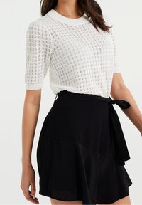 Haut en tricot blanc à manches courtes et col rond, associé à une jupe portefeuille noire avec un ourlet volé.