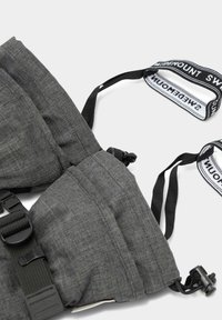 Imbracatura in tessuto Grigio con cinturini regolabili e una fibbia in plastica. Presenta dettagli di cucitura e una branding a strappo in bianco e nero contrastante.