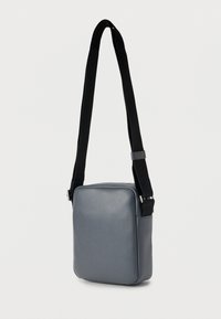 Γκρι δερμάτινη τσάντα φοδραρισμένη με τετράγωνο σχέδιο, με μαύρο ρυθμιζόμενο λουρί και ασημένιες μεταλλικές λεπτομέρειες. Λεπτή υφή, μίνιμαλ στυλ.