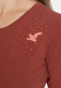 Rode katoenen t-shirt met een V-hals ontwerp, met een verloop van lichte spikkels en een silhouet van een vogel gedrukt op de schouder.