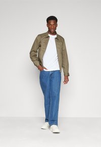 Šviesiai žalios spalvos, lengvas džemperis su apykakle, dėvimas ant balto marškinėlio ir mėlynų džinsų, derinamas su baltomis sportinėmis bateliais.