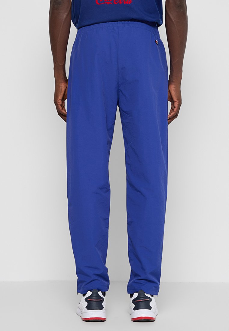 Pantalon bleu léger avec taille élastique et coupe fuselée. Fabriqué dans un tissu lisse, avec des poches latérales. Associé à des baskets blanches.