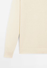 Pull en maille couleur crème à manches longues avec poignets et ourlet côtelés, présenté de profil sur un fond blanc uni.