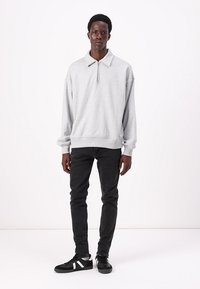 Sweatshirt cinza-claro com gola de fecho de correr até um quarto, combinado com jeans pretos e ténis pretos com detalhes brancos. Corte simples e relaxado.