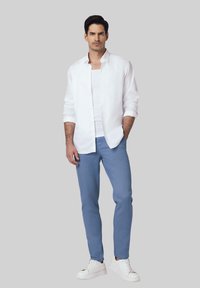 Biała koszula zapinana na guziki noszona na białym topie na ramiączkach, zestawiona z jasnoniebieskimi spodniami i białymi trampkami. Świeża tkanina o luźnym kroju.