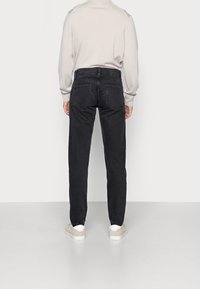 Svarta jeans i denim med rak passform, femficksdesign och subtil textur, kombinerade med en ljus tröja och beige skor.