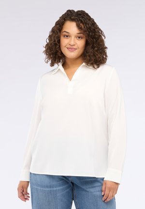Blusa bianca a maniche lunghe con colletto, tessuto morbido, vestibilità comoda e dettagli con bottoni su colletto e polsini. Abbinata a jeans.