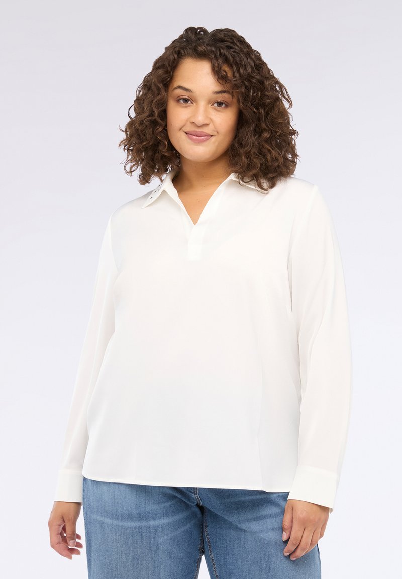Blusa bianca a maniche lunghe con colletto, tessuto morbido, vestibilità comoda e dettagli con bottoni su colletto e polsini. Abbinata a jeans.