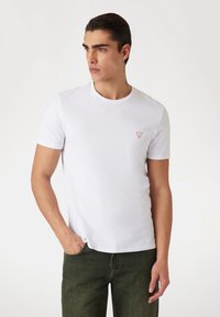 Hvid kortærmet t-shirt med rund halsudskæring og et lille rødt trekantet logo på venstre bryst; glat bomuldsstof.