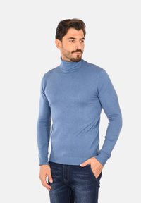 Pullover a collo alto di color azzurro chiaro, realizzato in materiale a maglia liscia, design aderente, con polsini e orlo a coste, indossato con jeans scuri.