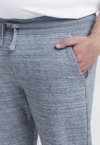 Sive, teksturirane trenirka hlače s pojasom na vezanje i bočnim džepovima, s mekanim materijalom i opuštenim krojem.