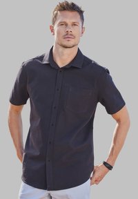 Chemise à manches courtes, de couleur bleu marine foncé, avec un bouton devant et une poche poitrine. Fabriquée en tissu léger avec une texture douce et une coupe décontractée.