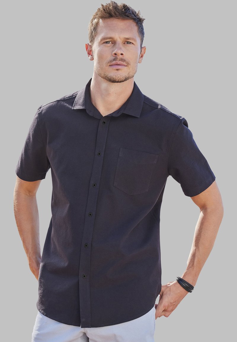 Chemise à manches courtes, de couleur bleu marine foncé, avec un bouton devant et une poche poitrine. Fabriquée en tissu léger avec une texture douce et une coupe décontractée.