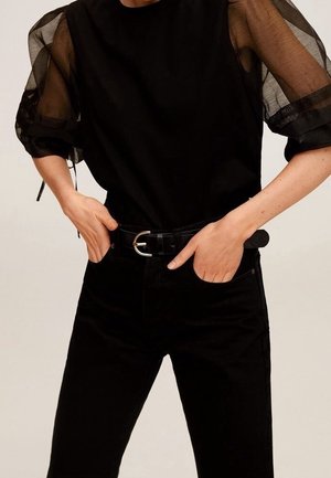 Zwarte top met doorschijnende pofmouwen, gecombineerd met zwarte high-waisted jeans en een zwarte riem met een ronde zilveren gesp.