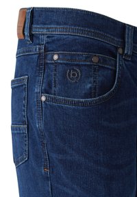 Dark blue denim jeans with front and side pockets, metal rivets, and a brown leather patch on the waistband.