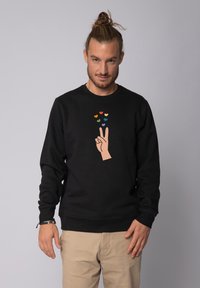 Black sweatshirt made of soft material featuring a cream hand sign with colorful hearts above it as the central graphic. Standard fit.