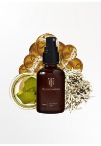 Bottiglia di vetro marrone con un tappo spray nero, etichettata "True Botanicals renew Nutrient Mist", circondata da gocce di olio dorato e foglie secche.