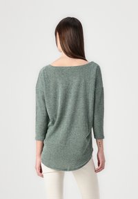 Groene gebreide top met een brede halslijn, driekwartmouwen en een afgeronde zoom. Gestructureerde stof voegt diepte toe aan het ontwerp.