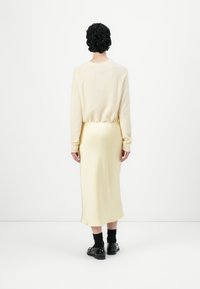 Cream knit sweater with long sleeves and ribbed cuffs, paired with a fitted yellow satin skirt. Black socks and chunky shoes complete the look.