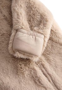 Beige fuskindsstof med en blød, fluffy tekstur. Har en strækbar stofmanchet ved enden, der giver varme og komfort.
