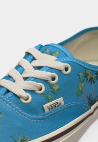 Baskets Vans bleues avec lacets blancs, petit imprimé floral et étiquette visible avec le logo Vans près des œillets sur le côté.