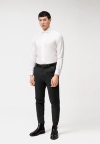 Weißes Hemd mit Knopf-Front, kombiniert mit dunklen, schmalen Hosen und schwarzen Leder-Stiefeletten. Glattes Material, strukturiertes Design.