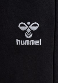White embroidered stylized bee logo above the word "hummel" on black fabric background.