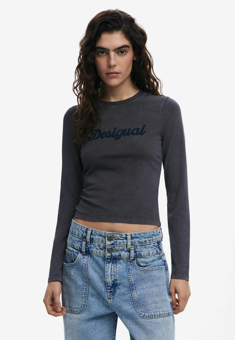 Dlhý rukáv šedý top s tmavomodrým logom "Desigual". Skrátený strih, hladká textúra. Nosí sa s svetlomodrými riflami s vysokým pásom.