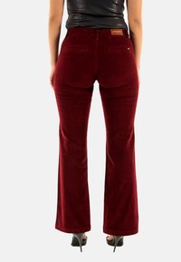 Pantaloni a zampa d'elefante in corduroy borgogna con tasche posteriori e etichetta in vita. Tessuto liscio e vestibilità sagomata con una leggera elasticità.