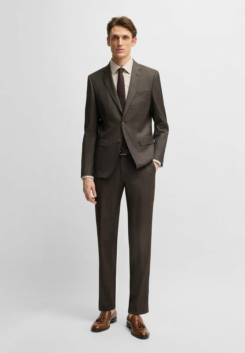 Brown tailored suit with a textured finish, a single-breasted jacket, notched lapels, and flat-front pants. Complimented by a light shirt and dark tie.