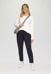 Witte, lange mouwen trui, donkerblauwe broek en witte sneakers. Accessoire: kleine grijze crossbody tas. Glad textuur, casual pasvorm.