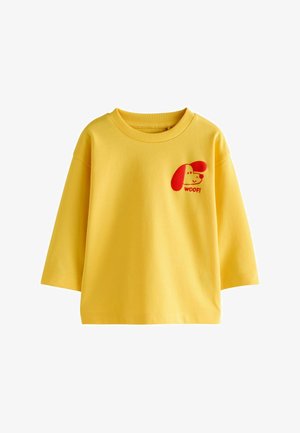 Geel shirt met lange mouwen met rood cartoon hondenhoofd en de tekst "WOOF!" op de linker bovenborst.