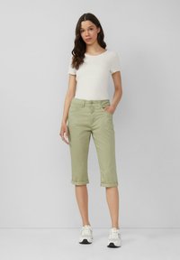 Jasnozielone spodnie typu cropped z podwiniętymi mankietami, w połączeniu z białą, teksturowaną bluzką z okrągłym dekoltem i białymi sneakersami. Gładki materiał, swobodny fason.