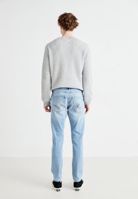 Pull en maille côtelée gris clair, jean bleu clair avec détails au dos, chaussures noires. Design simple et décontracté avec un tissu texturé et une coupe relaxée.
