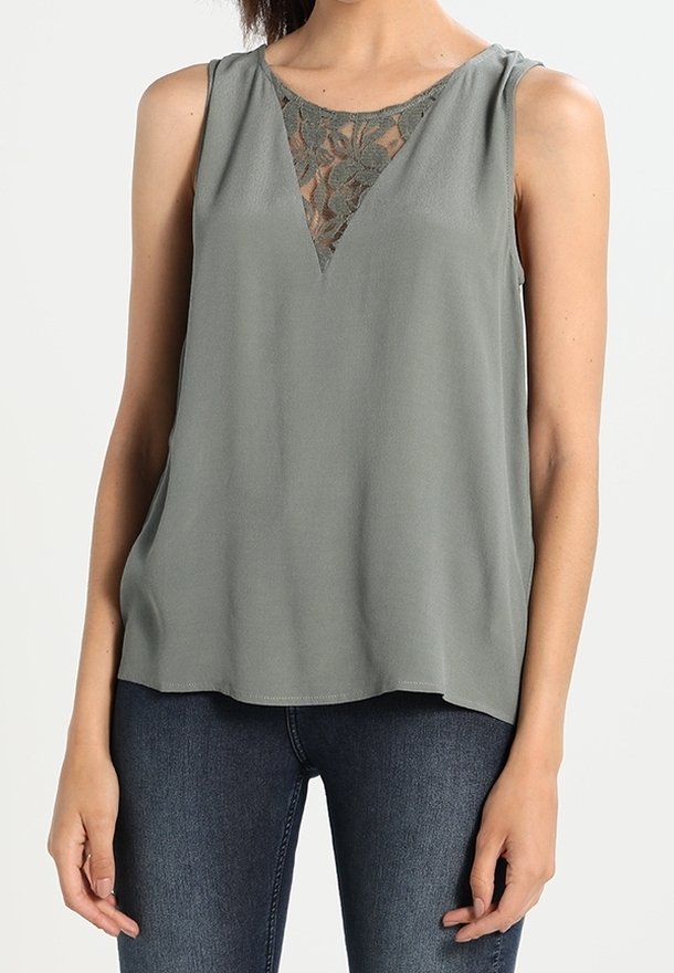 Haut sans manches en vert doux, avec un décolleté en V orné de dentelle. Tissu doux avec une coupe fluide, associé à un jean en denim foncé.