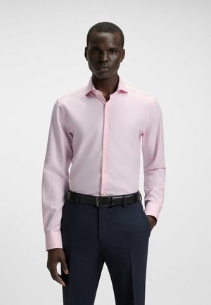 Lichtroze overhemd met lange mouwen en een button-down kraag, met een geruit patroon. Draagt met een donkere broek en een zwarte riem.
