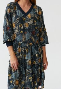 Vestido con estampado floral que presenta una base azul marino con hojas y flores coloridas, un escote en V y un dobladillo de volantes en varias capas.