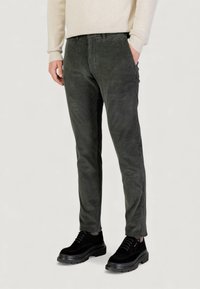 Pantaloni verde scuro in velluto a coste con vestibilità aderente, caratterizzati da costine verticali, tasche laterali e vita elastica. Indossati con scarpe platform nere.