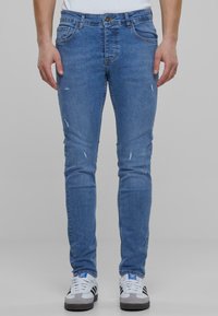 Világoskék, slim fit farmernadrág, térdnél kopással, öt zsebbel és egy gombos derékzárral.