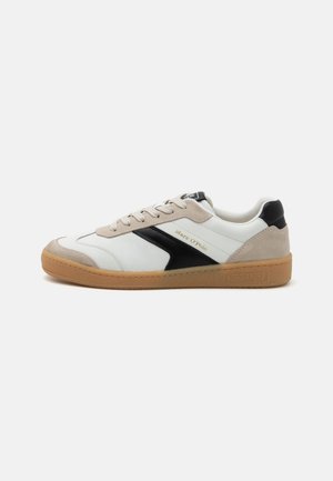 White and black sneaker with beige accents, made of leather and suede. Features textured gum sole and branding on the side. Low-top design.
