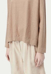 Ljusbrun, strukturerad långärmad topp med avslappnad passform och en något längre bakre fåll, i kombination med krämfärgade, plisserade shorts.