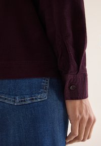 Bordeaux kordfløjlskjorte med knapmanchetter, tekstureret stof, parret med blå denim jeans med kontrastsyninger og detaljer på baglommen.
