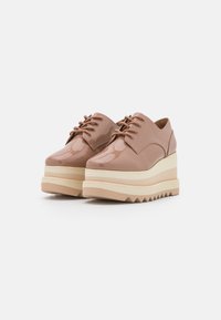 Chaussures à plateforme à lacets en cuir verni beige brillant avec une semelle superposée crème et des bords dentelés, dotées d'un bout arrondi et de coutures discrètes.