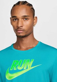 Camiseta deportiva turquesa de manga corta, con un gran texto en neón verde "RUN" y el logo de Nike. Textura de tela suave.