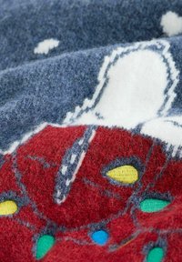 Dettaglio di un maglione lavorato a maglia con un motivo rosso e accenti gialli, verdi e blu, su uno sfondo blu grigio. Tessuto morbido e texturizzato.