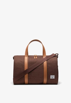 Sac de sport en tissu marron avec des accents et des poignées en cuir beige. Il dispose d'une fermeture par zip sur le dessus et d'une bandoulière amovible.