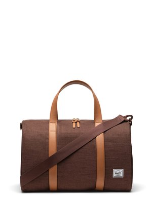 Sac de sport en tissu marron avec des accents et des poignées en cuir beige. Il dispose d'une fermeture par zip sur le dessus et d'une bandoulière amovible.