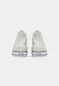 Hvite lær høye sneakers med rund tå, teksturert overflate og svart-hvitt gummisåle med "Converse All Star" logo.