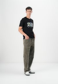 Black T-shirt with colorful "JACK & JONES" logo, paired with olive green pants. White sneakers complete the outfit. Simple design, casual look.